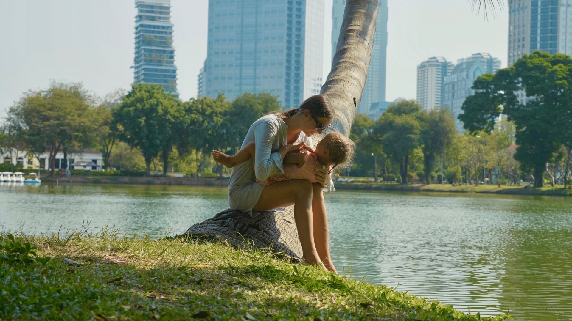 A mother and her child sit on a tree overlooking the pond in Lumpini Park